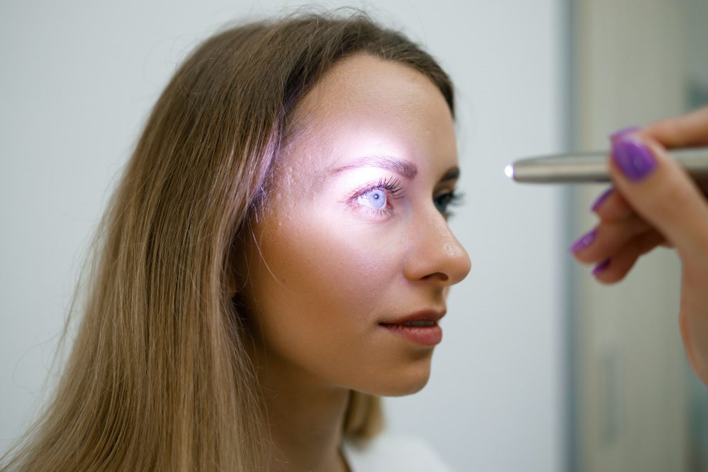 Close up view of doctor testing reflexes of the eye of young woman using a flashlight