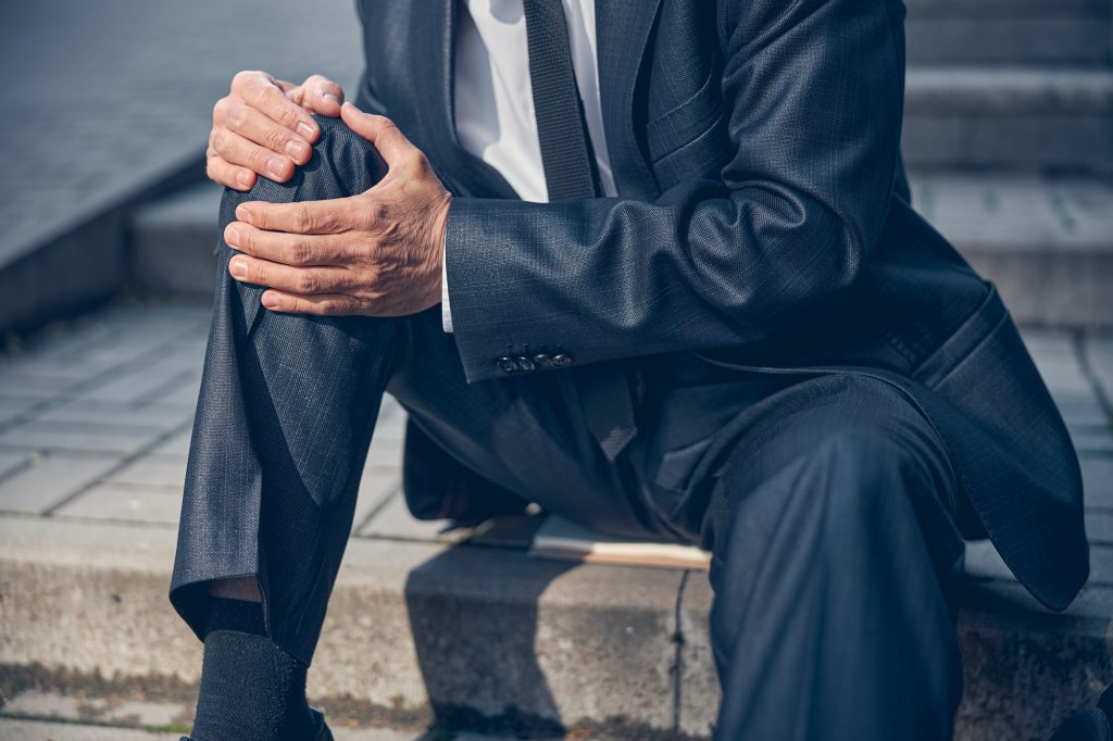 Man in suit suffering from knee pain on the street