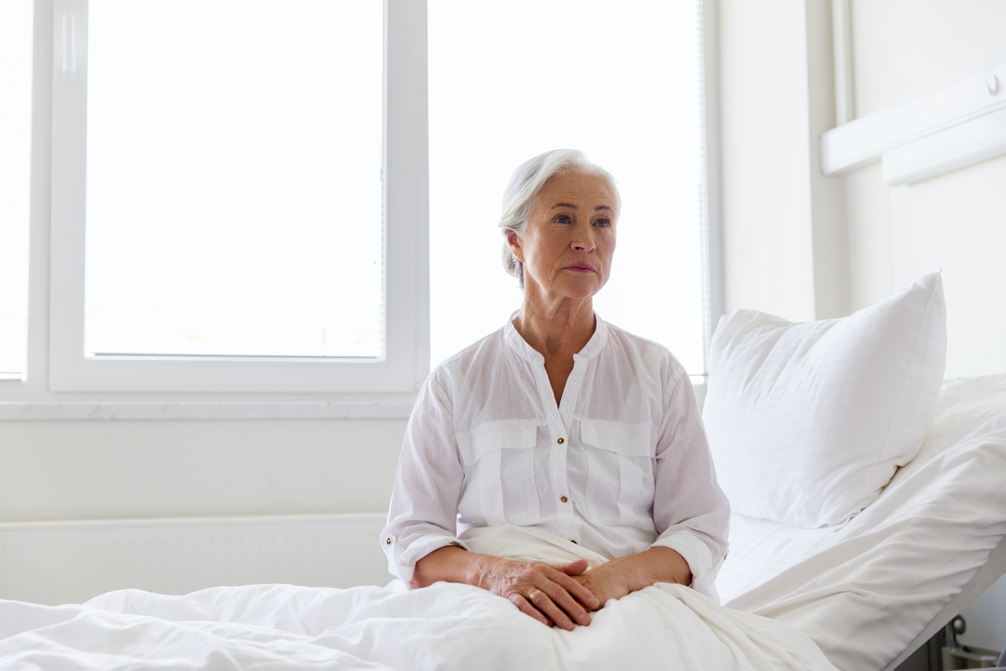 sad senior woman sitting on bed at hospital ward