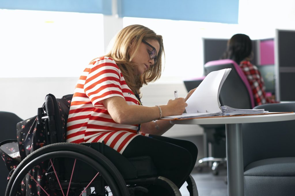 Teenage girl in wheelchair writing up notes in class