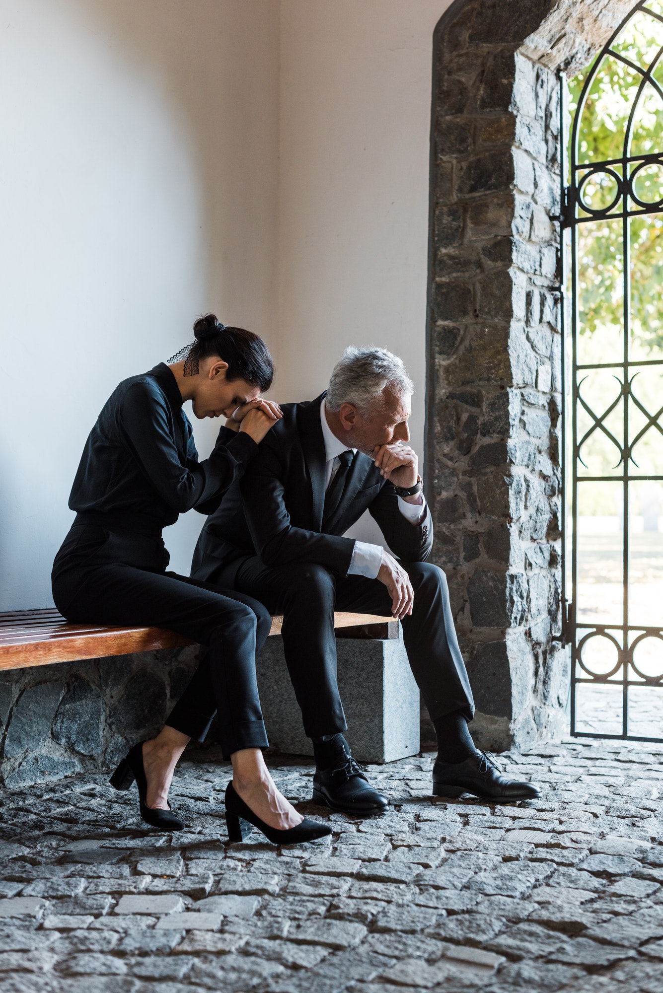 upset woman and sad man sitting on bench on funeral