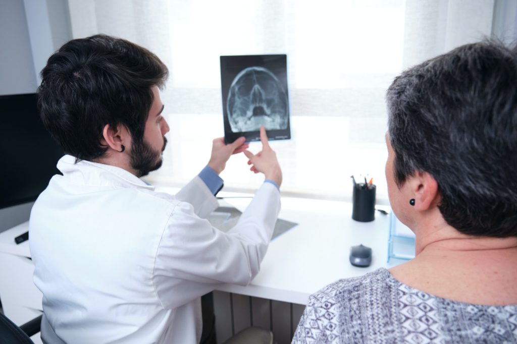 Young doctor examining x-ray of the skull, sinuses with a mature woman patient